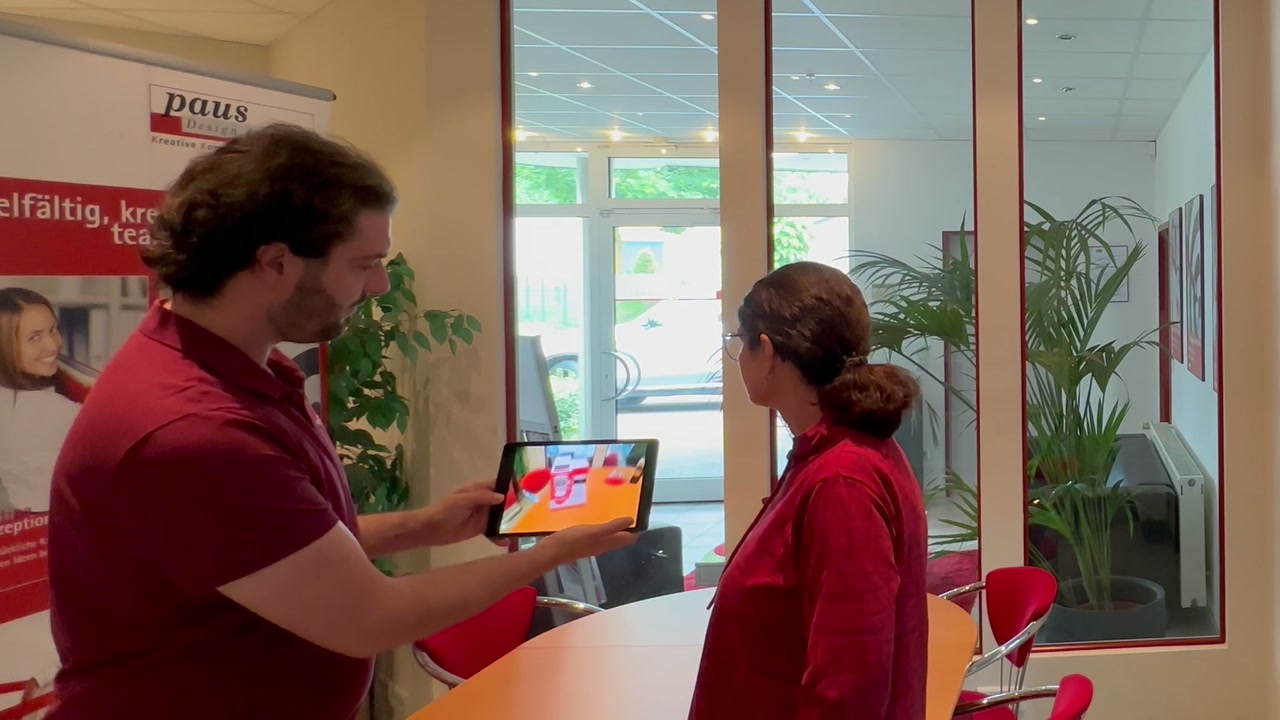 Kundentermin im Besprechungsraum: Ein Berater zeigt einer Kundin auf dem iPad eine Kaffeemaschine in Augmented Reality