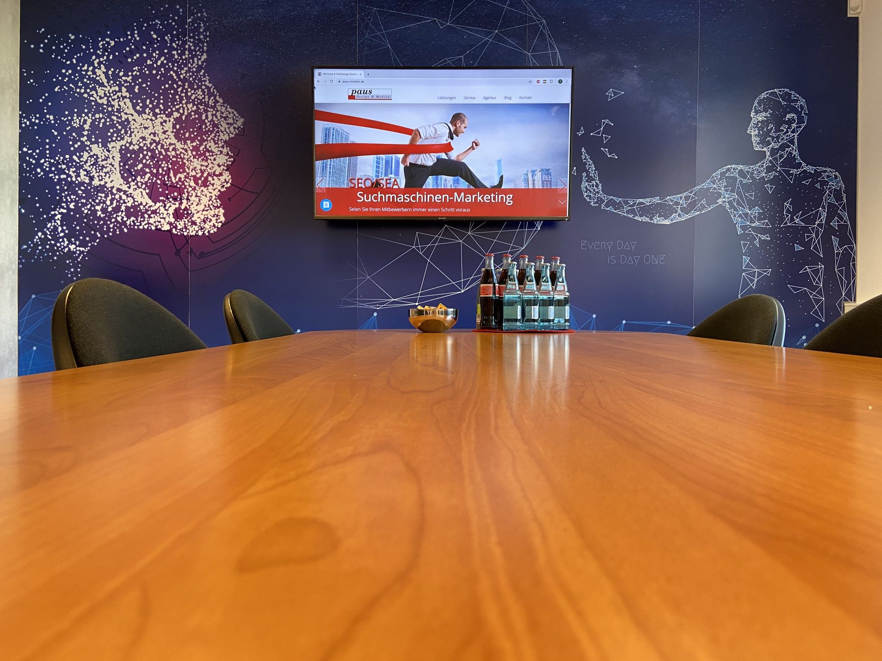 Besprechungsraum der Agentur mit langem Holztisch, auf dem Bildschirm eine Folie zum Suchmaschinen-Marketing