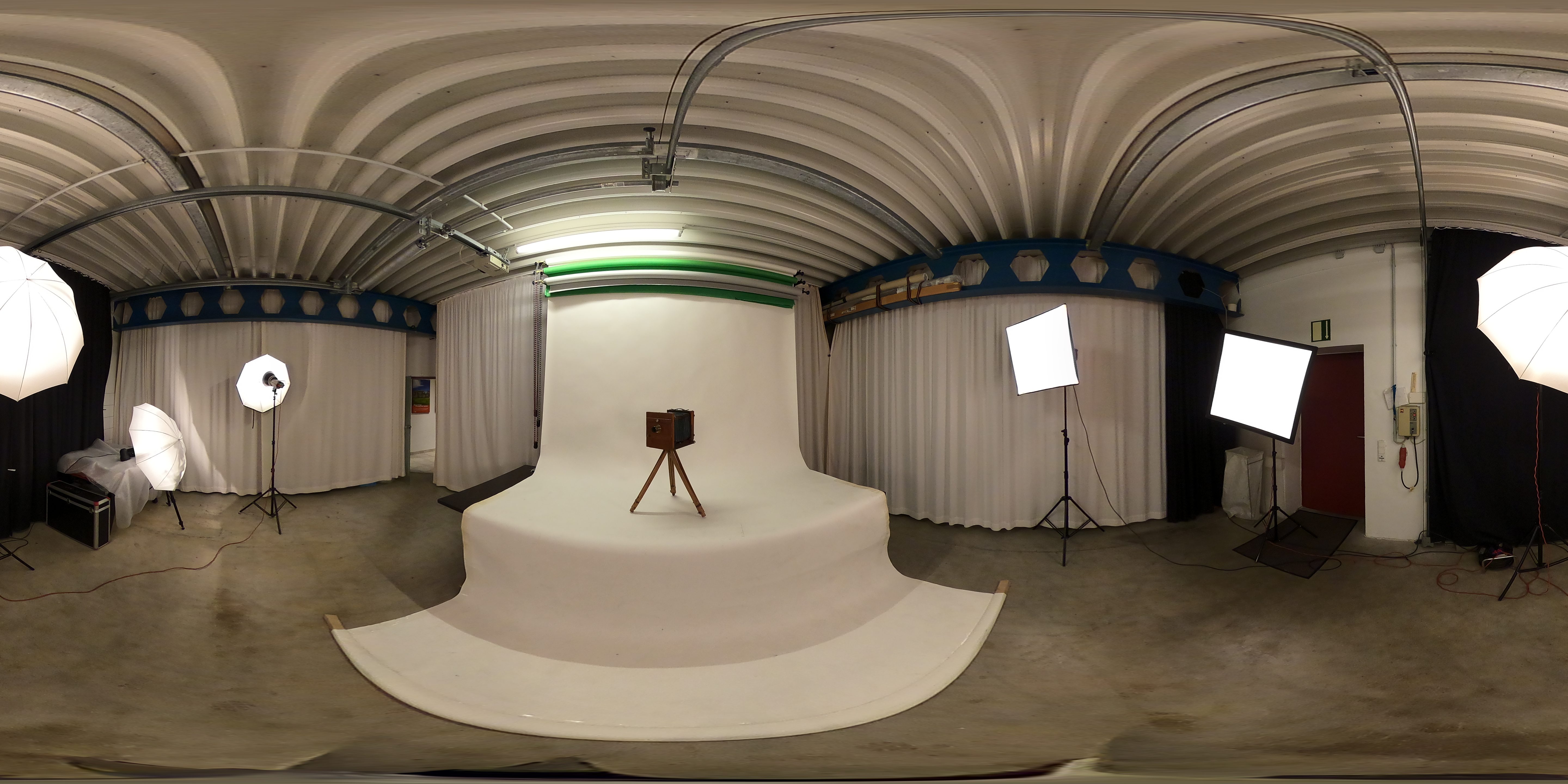 Rundumfoto des Fotostudios der Agentur mit weißer Hohlkehle, Softboxen, Schirmen, Vorhängen und einer alten Plattenkamera auf einem Holzstativ