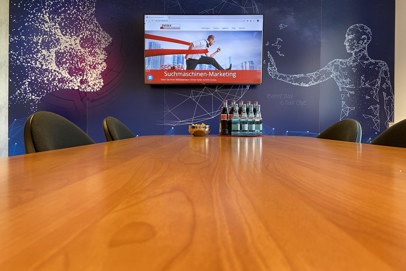 Besprechungsraum der Agentur Paus: langer Holztisch, an der Wand ein Bildschirm mit einer Folie zum Suchmaschinen-Marketing