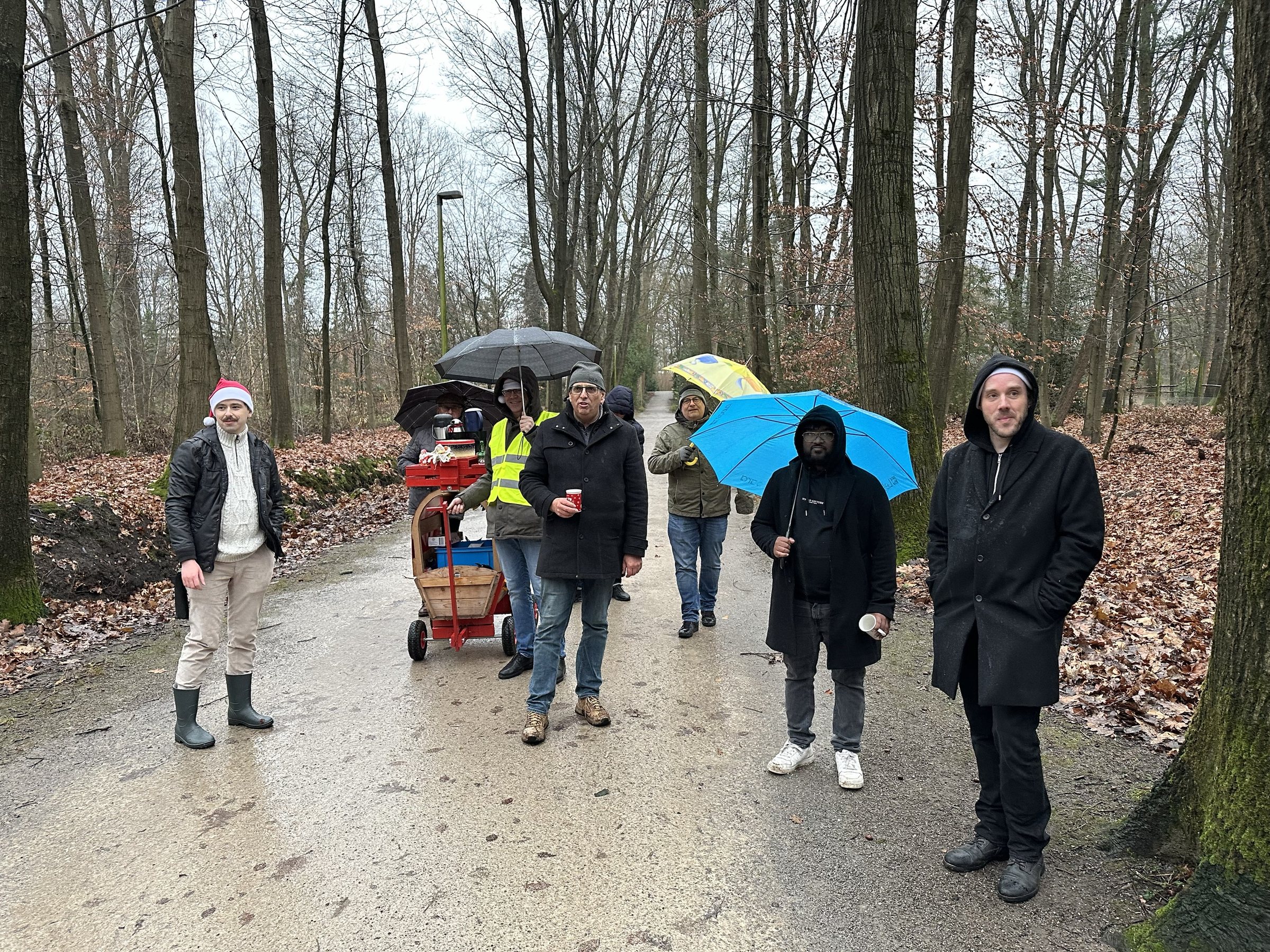 Das Team von Paus Design und Medien beim Bosseln auf einem Waldweg, mit Bollerwagen und bunten Regenschirmen