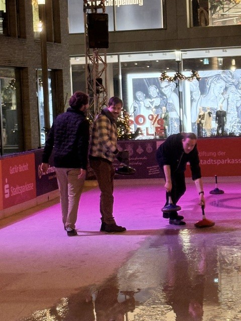 Das Team an der Eisstockbahn, ein Kollege bringt den Eisstock auf den Weg