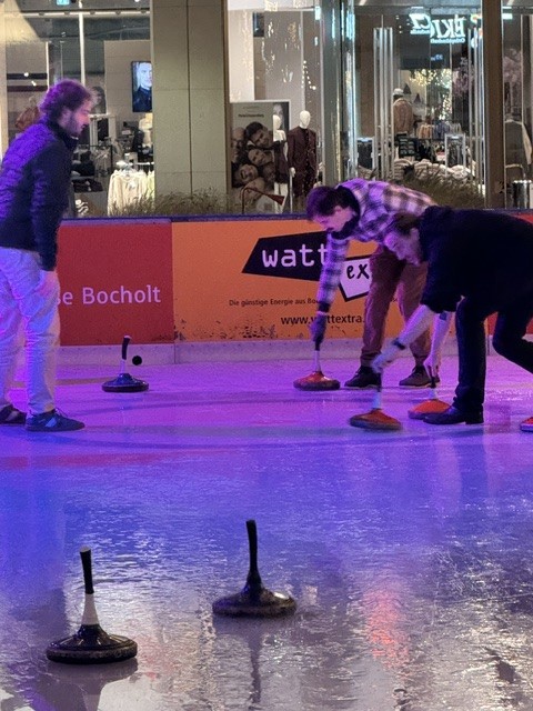 Drei Kollegen beim Eisstockschießen auf der Eisbahn in Bocholt, einer setzt gerade zum Wurf an