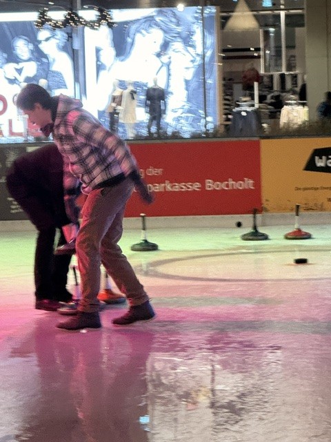 Zwei Kollegen beugen sich beim Eisstockschießen über die Bahn