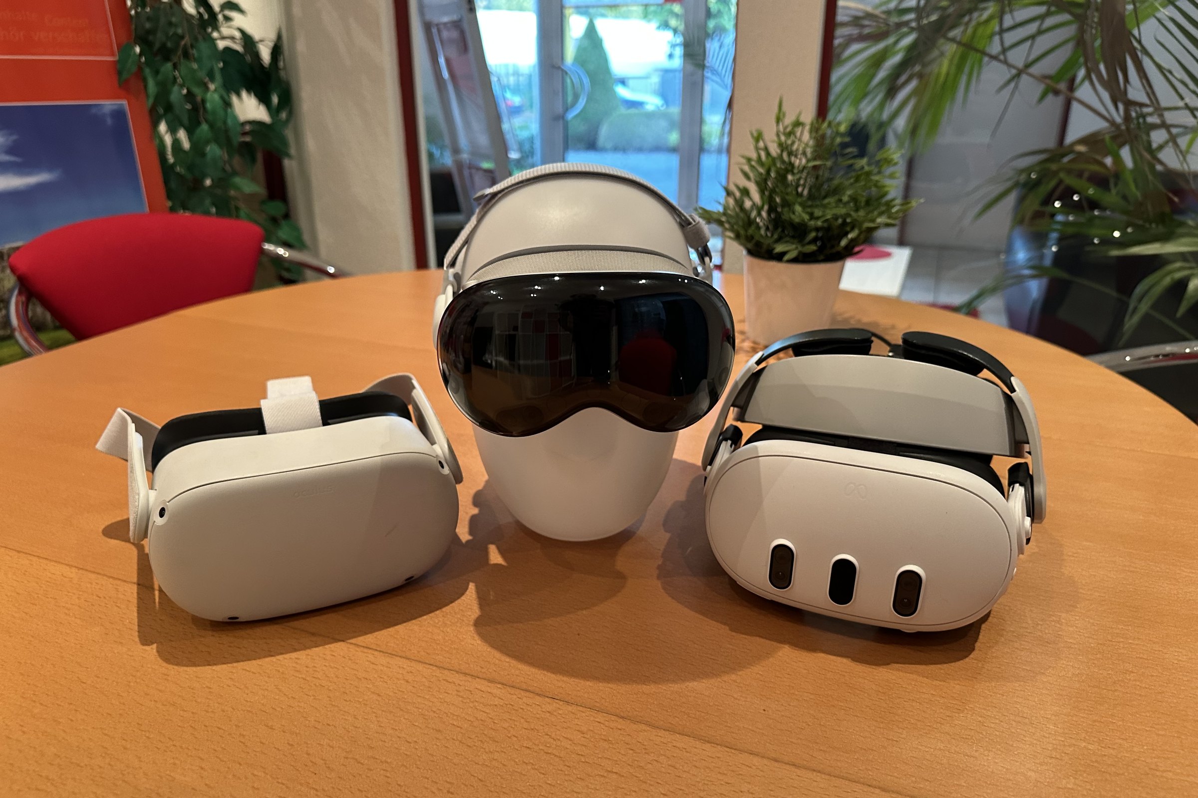 Drei Brillen auf dem runden Tisch im Empfang der Agentur: links eine Meta Quest 2, in der Mitte eine Apple Vision Pro auf einer Kopfbüste, rechts eine Meta Quest 3