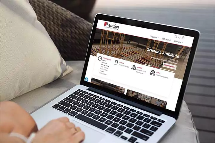 Laptop auf einem Sofa zeigt die Startseite des Online-Shops von Hemsing textil mit stil