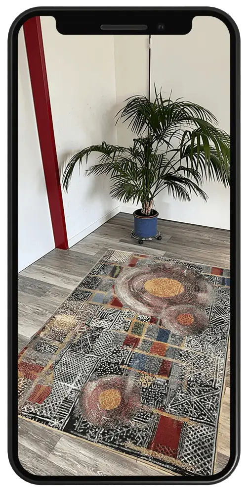 Smartphone zeigt einen bunt gemusterten Teppich in Augmented Reality auf dem Holzboden einer Zimmerecke mit Palme