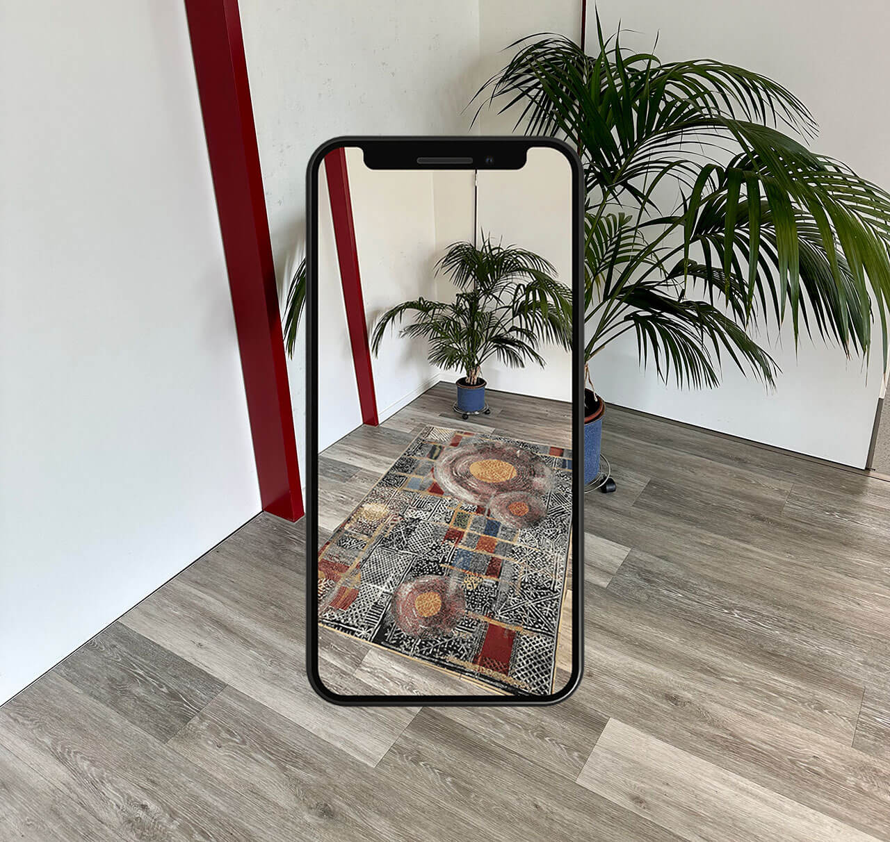 Smartphone vor einer Zimmerecke mit Palme, auf dem Display liegt ein bunt gemusterter Teppich in Augmented Reality auf dem Holzboden
